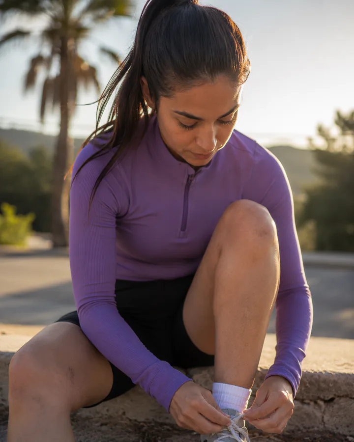 Runner in purple sportswear tying her shoes outdoors