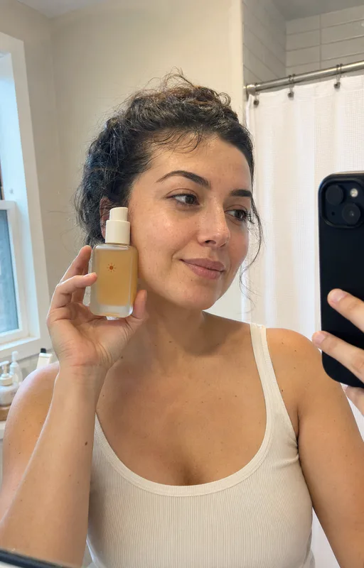 Customer holding skincare serum in a bathroom mirror selfie